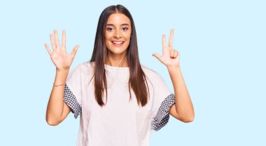 Genç İspanyol kadın gündelik kıyafetler giyer ve sekiz numaralı parmaklarıyla gülümseyerek mutlu ve kendinden emin bir şekilde işaret eder.. 