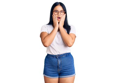 Genç ve güzel Asyalı kız günlük kıyafetler ve gözlük takıyor. Korkuyor ve şoka uğruyor. Şaşırıyor ve şaşırıyor. 