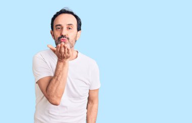 Orta yaşlı, sıradan tişörtler giyen yakışıklı bir adam kameraya bakıp havada el sallayarak öpüşüyor ve güzel ve seksi oluyor. aşk ifadesi. 