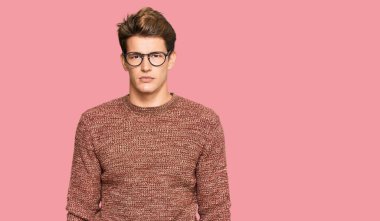 Yakışıklı, beyaz bir adam günlük süveter giyiyor ve yüzünde ciddi bir ifade olan gözlük takıyor. Basit ve doğal bir şekilde kameraya bakıyorsun.. 