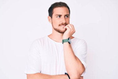 Gündelik beyaz tişört giyen genç yakışıklı. Stresli ve gergin görünüyor. Elleri ağızdan tırnak yiyor. anksiyete. 