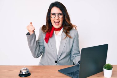 Genç, güzel esmer kadın otel resepsiyonunda çalışırken dizüstü bilgisayar kullanarak gururla bağırıyor, zaferi kutluyor ve kollarını kaldırarak çok heyecanlanıyor. 