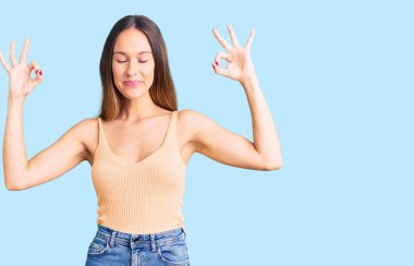 Güzel, esmer, günlük kıyafetler giyen genç bir kadın. Rahat ol ve gülümse. Gözlerin kapalı, parmaklarınla meditasyon yap. yoga konsepti. 