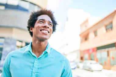 Genç, yakışıklı, Afro-Amerikan bir adam günlük giysiler giyip mutlu gülümsüyor. Yüzünde tebessümle kasaba caddesinde yürürken yan tarafa bakıyor..
