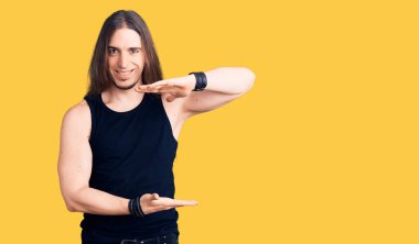 Uzun saçlı, gotik tarzda giyinen, siyah elbiseli, elleri büyük ve büyük boy işareti olan genç bir adam. Kameraya bakıp gülümsüyor. ölçüm kavramı. 