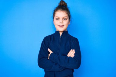 Sıradan kıyafetler giyen sevimli İspanyol çocuk kollarını kavuşturup kameraya bakarken gülümsüyor. pozitif kişi. 