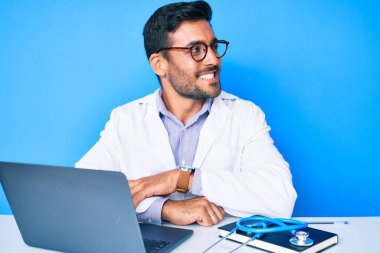 Klinikte çalışan, doktor üniforması giyen genç İspanyol bir adam. Profil oluşturmaya çalışıyor. Doğal bir yüzü ve kendine güvenen bir gülümsemesi var.. 