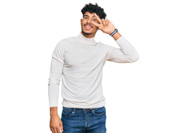 Gündelik kazak giyen genç Arap adam barış sembolü yapıyor. Yüzünde parmaklar, gülümseyerek zaferi gösteriyor. 