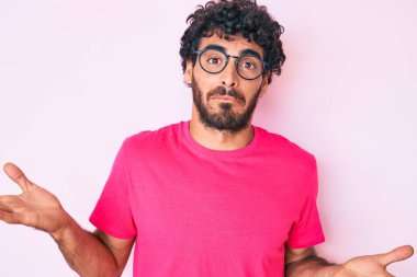 Kıvırcık saçlı, ayılı, sıradan kıyafetler giyen, gözlüksüz, kafası karışmış, elleri ve kolları havada yakışıklı bir genç. şüphe kavramı. 