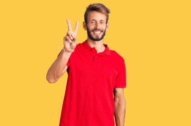 Yakışıklı, sakallı, sıradan kıyafetler giyen, iki numaralı parmaklarıyla işaret eden, kendinden emin ve mutlu bir adam.. 