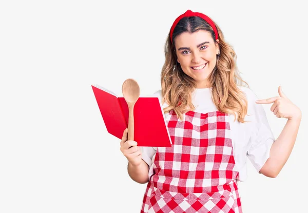 Νεαρή Καυκάσια Γυναίκα Που Φοράει Ποδιά Κρατώντας Βιβλίο Συνταγών Και — Φωτογραφία Αρχείου