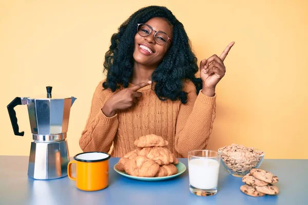 美しいアフリカの女性は テーブルの上に座って朝の笑顔で朝食を食べ カメラを見て2本の手と指で側面を指して — ストック写真