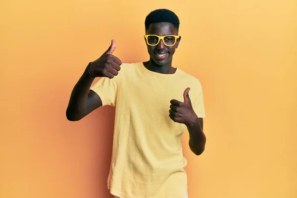 年轻的非洲裔美国人 身穿休闲装 戴着眼镜 赞成用手做积极的手势 微笑着竖起大拇指 为成功感到高兴 优胜手势 — 图库照片