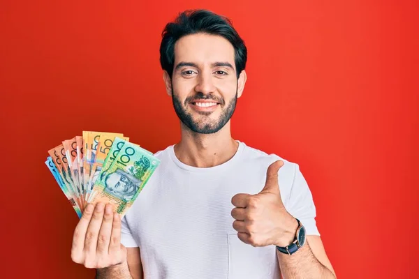 Joven Hombre Hispano Sosteniendo Dólares Australianos Sonriendo Feliz Positivo Pulgar — Foto de Stock