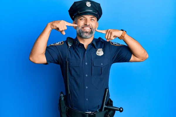 Middle age handsome man wearing police uniform smiling cheerful showing and pointing with fingers teeth and mouth. dental health concept.