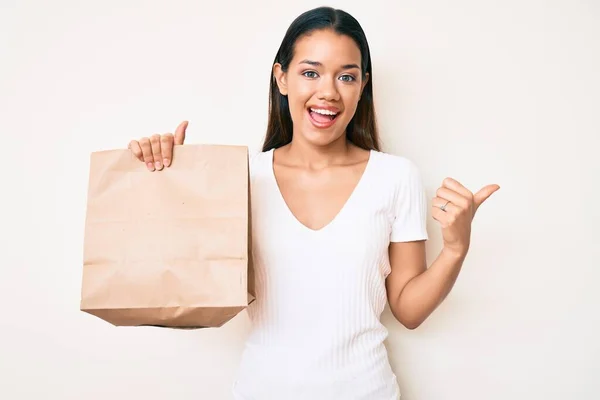 Joven Hermosa Chica Latina Sosteniendo Llevar Bolsa Papel Apuntando Pulgar —  Fotos de Stock