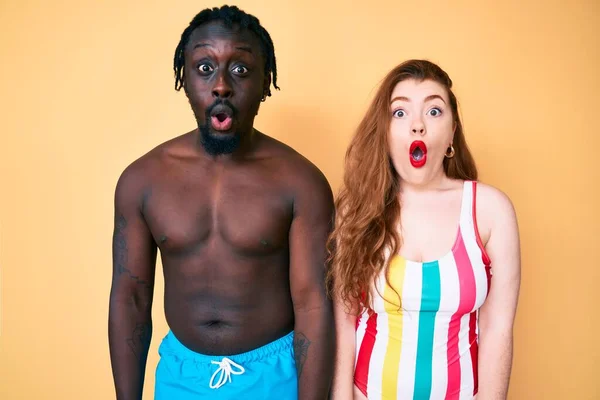 Interracial couple wearing swimwear afraid and shocked with surprise expression, fear and excited face.