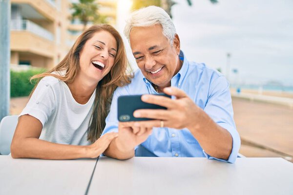 Влюбленная пара среднего возраста, сидящая на террасе кофейни, используя смартфон счастливыми и веселыми вместе
