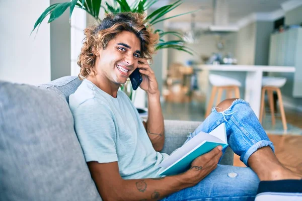Joven Hombre Hispano Sonriendo Feliz Hablando Teléfono Inteligente Leyendo Libro —  Fotos de Stock