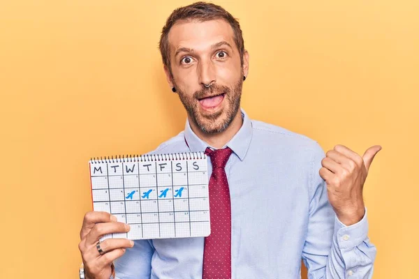 Young Handsome Man Holding Travel Calendar Pointing Thumb Side Smiling — Stock Photo, Image