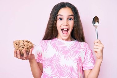 Tatlı İspanyol kız elinde mısır gevreği ve kaşık tutarak çılgınlığı kutluyor ve başarı için hayrete düşmüş gözleri açık heyecanla bağırıyor.. 