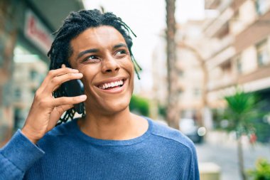 Genç Afrikalı Amerikalı gülümseyen mutlu bir adam şehrin caddesinde akıllı telefondan konuşuyor..