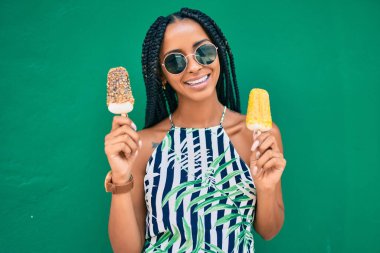 Genç Afrikalı Amerikalı kadın gülümseyerek şehirde dondurma yiyor..