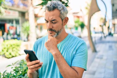 Şehrin caddesinde akıllı telefon kullanan, orta yaşlı, gri saçlı bir adam ciddi bir yüz ifadesi olan, eli çenesinde soru soran, kafa karıştırıcı bir fikir hakkında düşünceli biri. 