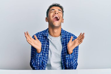 Genç ve yakışıklı Afro-Amerikan adam, gündelik giysiler içinde masada oturmuş başarıyı kutlarken kolları havada ve gözleri kapalı heyecanlı bir şekilde çığlık atıyor. Kazanan konsept 