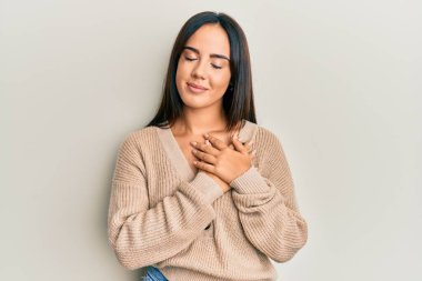 Kış süveteri giymiş, elleri göğsünde gülümseyen, güzel İspanyol bir kız. Minnettar bir yüz ifadesiyle gözleri kapalı. sağlık kavramı. 