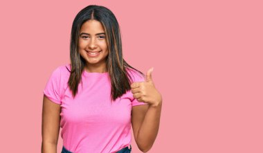 Gündelik kıyafetler giyen genç Latin kız elinle mutlu bir jest yapıyor. Kameraya bakıp başarıyı gösteren ifade. 