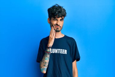 Gönüllü tişört giyen genç İspanyol adam diş ağrısı ya da diş hastalığından dolayı acı dolu bir ifadeyle ağıza dokunuyor. dişçi kavramı. 