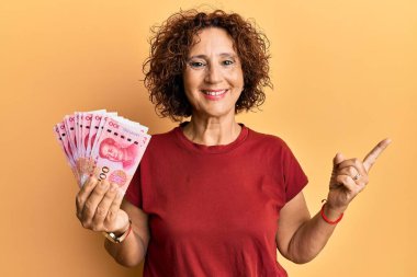 Güzel orta yaşlı bir kadın elinde 100 yuan Çin banknotuyla mutlu bir şekilde gülümsüyor. 
