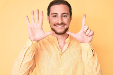 Genç ve yakışıklı bir adam gündelik giysiler giyer ve yedinci parmaklarını göstererek gülümserken kendinden emin ve mutlu olur.. 