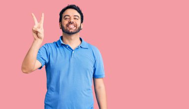 Gündelik kıyafetler giyen genç İspanyol adam iki numarayı gösterip işaret ederken kendinden emin ve mutlu bir şekilde gülümsüyor.. 