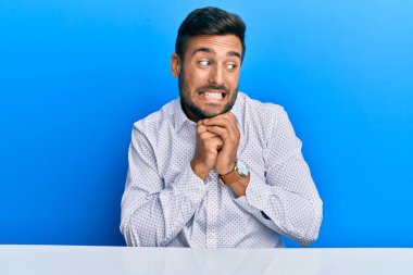 İş kıyafetleri giymiş yakışıklı İspanyol bir adam masaya oturmuş gergin ve heyecanlı bir şekilde çenesinin kenarına bakıyor. 