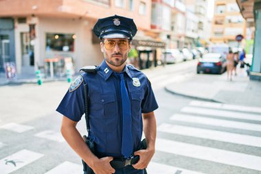 Polis üniforması giyen genç, yakışıklı İspanyol polis. Kasaba caddesinde ciddi bir ifadeyle dikiliyorsun..