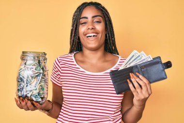 Tasarruf kavanozu ve cüzdanı olan, gülümseyen ve kahkahalarla kahkahalarla gülen genç Afrikalı Amerikalı bir kadın.. 