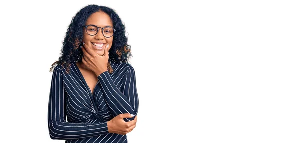カジュアルな服と眼鏡を身に着けている若いアフリカ系アメリカ人の女性は カメラを見て自信を持って交差腕とあごに提起手で笑っている ポジティブな — ストック写真