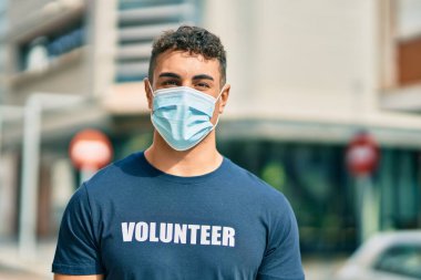 Şehirde duran tıbbi maske takan Latin kökenli gönüllü genç adam..