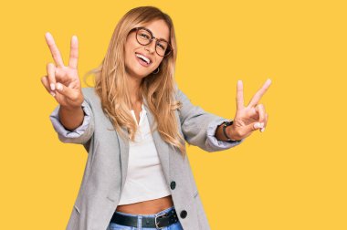 İş elbiseleri giymiş, ağzı açık gülümseyen güzel sarışın bir kadın zafer işareti yaparken parmaklarını gösteriyor. İki numara.. 