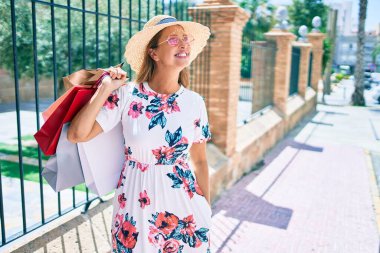 Orta yaşlı İspanyol kadın şehirde alışveriş torbalarını tutarken mutlu gülümsüyor.