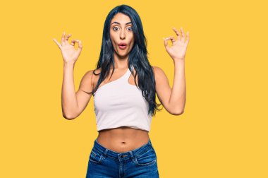Gündelik kıyafetler giyen güzel İspanyol kadın şaşırmış ve şok olmuş görünüyor. Tamam sembolünü parmaklarıyla yapıyor. çılgın ifade 