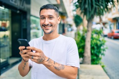 Şehrin caddesinde akıllı telefon kullanan, mutlu gülümseyen genç İspanyol adam..