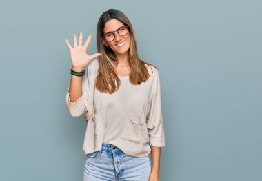 Gündelik kıyafetler giyen ve gözlük takan genç bir kadın beş numarayı gösterip işaret ederken kendinden emin ve mutlu bir şekilde gülümsüyor.. 