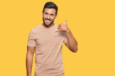 Yakışıklı, günlük kıyafetler giyen, gülümseyen, el ve parmaklarıyla telefon hareketi yapan telefonda konuşan bir İspanyol. iletişim kavramları. 