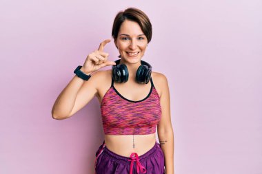 Kısa saçlı, kısa saçlı, spor giyimli, kulaklık takan, gülümseyen, kendine güvenen, el hareketleriyle küçük beden işareti yapan ve kameraya bakan esmer bir kadın. ölçüm kavramı. 