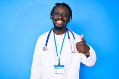 Doktor steteskopu ve kimlik kartı takan, gülümseyen, mutlu ve pozitif gülümseyen, mükemmel ve onay işareti olan Afro-Amerikan genç adam. 