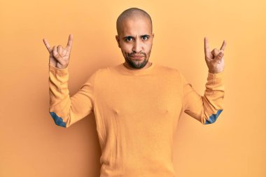 Latin kökenli yetişkin bir adam sarı arka plan şüphecisi ve gergin üzerine kaya hareketi yapıyor, sorun yüzünden surat asıyor. negatif kişi. 