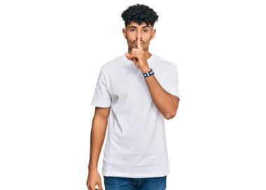 Gündelik beyaz tişört giyen genç bir Arap dudaklarında parmaklarıyla sessiz olmak istiyor. sessizlik ve gizli konsept. 